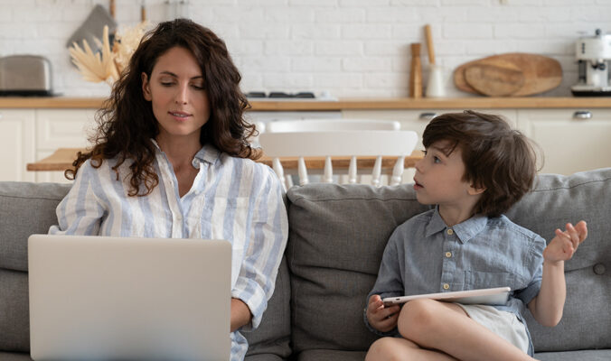 Woman working from home on a laptop, with small child next to her.